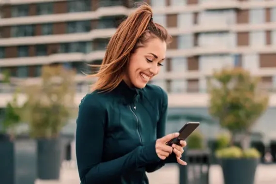 Imagem de uma mulher sorrindo e olhando para um smartphone.