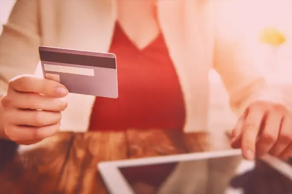 imagem de mão feminina segurando um cartão de crédito e a outra mão digitando em um tablet