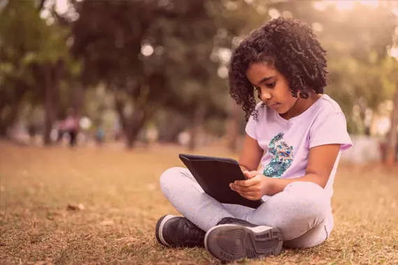 criança sentada em um ambiente ao ar livre olhando para um tablet